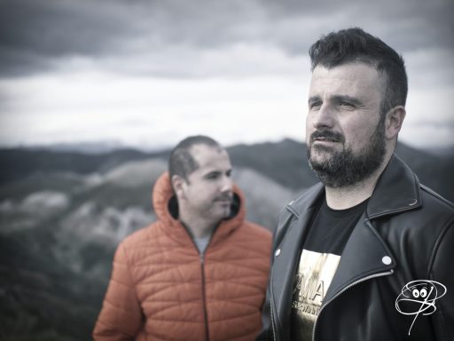 Dos hombres en la montaña, uno con chaqueta de cuero y otro con una chaqueta naranja.